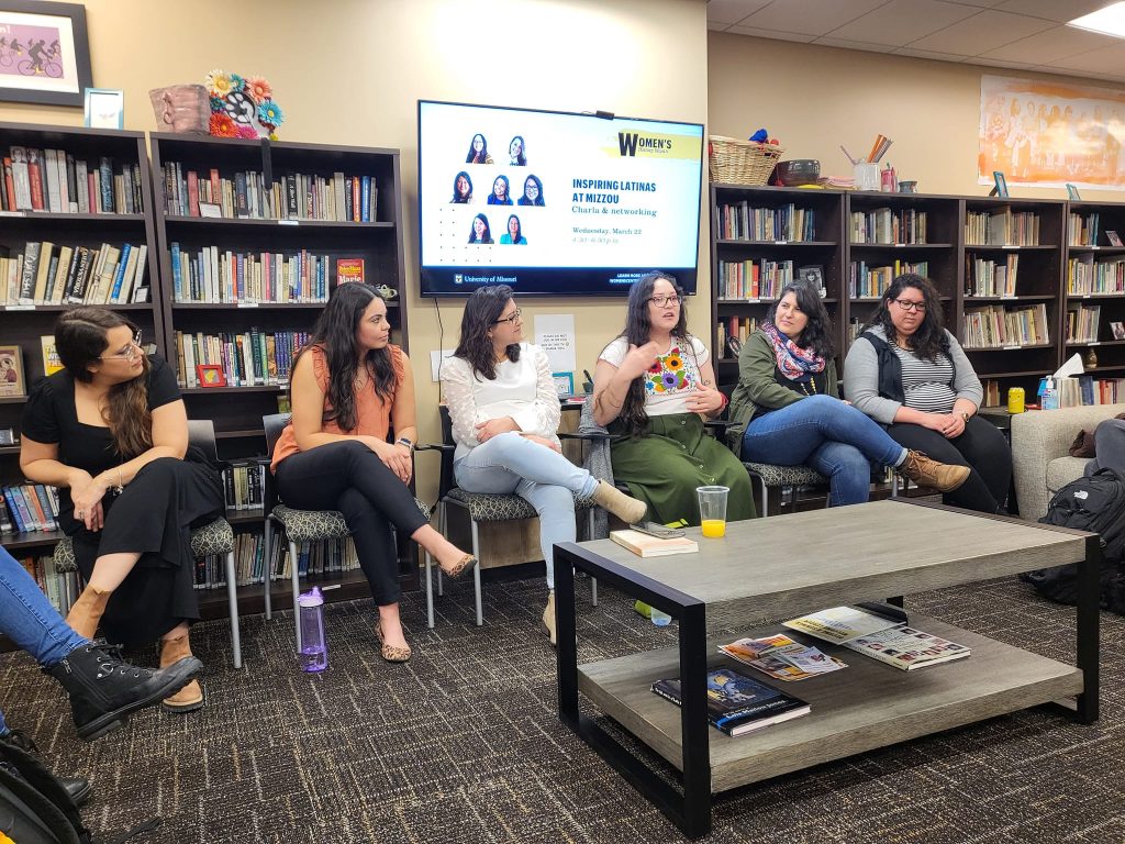 Image of 6 student latinas presenting at a panel. In the background a powerpoint presentation reads, "Inspiring Latinas at Mizzou",